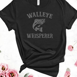 K&ouml;nnte beinhalten: Schwarzes T-Shirt mit dem Text "Walleye Whisperer" in grauer Schrift und einer grauen Silhouette eines Zanderfisches.