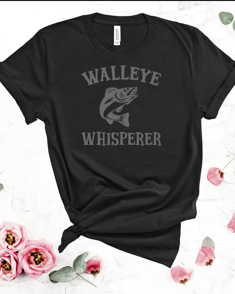 K&ouml;nnte beinhalten: Schwarzes T-Shirt mit dem Text "Walleye Whisperer" in grauer Schrift und einer grauen Silhouette eines Zanderfisches.