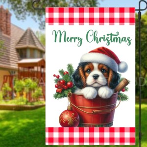 Op de afbeelding: Een tuinvaandel met een rood-witte geruite rand en de woorden "Merry Christmas" in groen schrift. De vlag toont een Cavalier King Charles Spaniel puppy met een kerstmuts, zittend in een rode emmer met kerstversieringen.