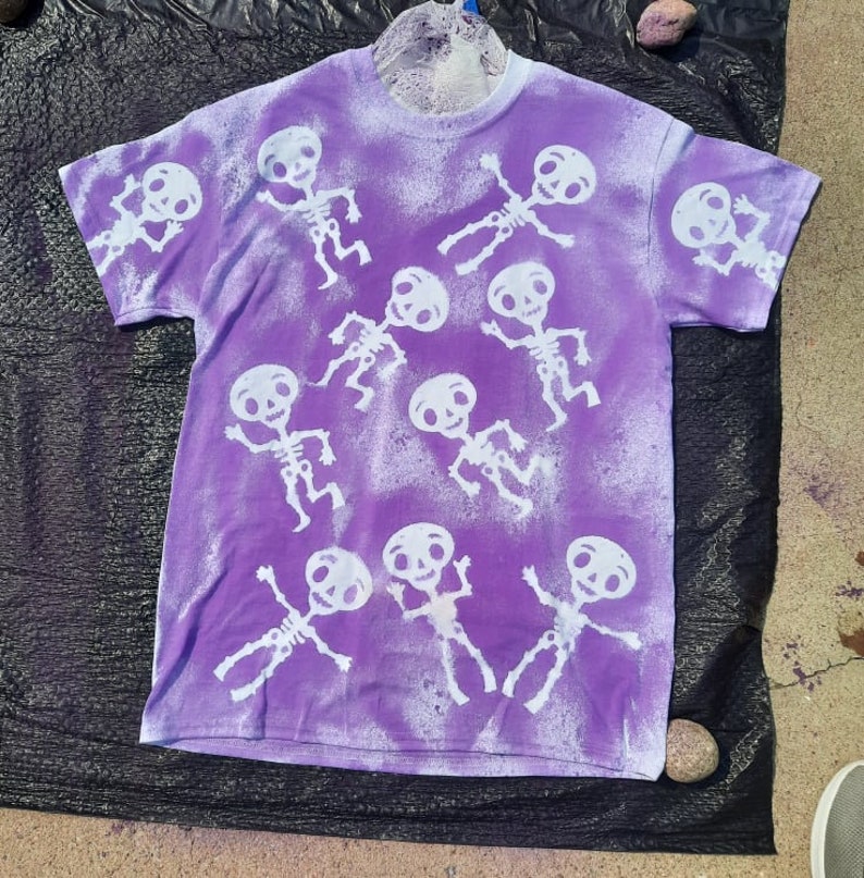 May include: Purple t-shirt with a white bleach design of skeletons dancing.