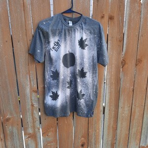 May include: A dark gray t-shirt with a bleach-splattered design featuring a pumpkin and maple leaves. The text "Hello Fall" is written on the shirt.