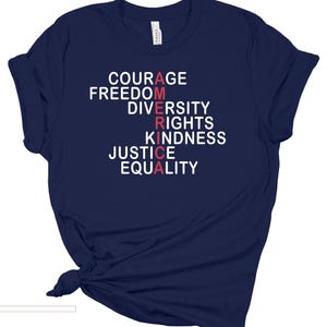 May include: Navy blue t-shirt with the word "AMERICA" spelled vertically in red and white letters. The words "COURAGE, FREEDOM, DIVERSITY, RIGHTS, KINDNESS, JUSTICE, EQUALITY" are printed above and below the word "AMERICA".