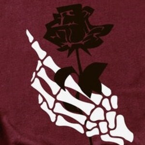 Peut inclure: Une main squelettique blanche tenant une rose noire avec une tige et des feuilles.
