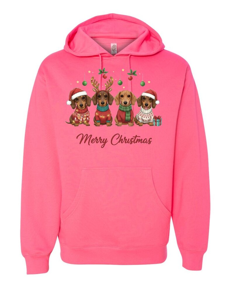 May include: A bright pink hoodie featuring a festive design. The graphic shows four dachshunds dressed in holiday attire, including Santa hats and sweaters, with the text "Merry Christmas" below. The hoodie has a front pocket and a hood.