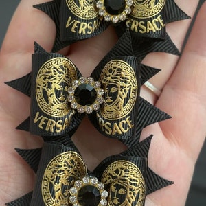 May include: Three black hair bows with gold Versace logos and black and clear rhinestones.