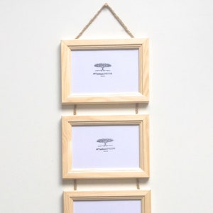 Peut inclure: Trois cadres photo en bois naturel sont suspendus verticalement à l'aide d'une ficelle. Chaque cadre a un passe-partout blanc et un petit logo d'arbre en bas au centre. Le logo indique "My Unique Decor".