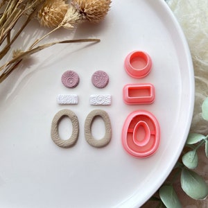 Op de afbeelding: Een set polymer clay oorbellen in roze, wit en bruin. De oorbellen worden gepresenteerd op een wit bord met roze en witte polymer clay uitstekers.
