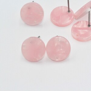 May include: A set of six pink round earrings with silver posts. The earrings are made of a translucent material with a marbled effect.
