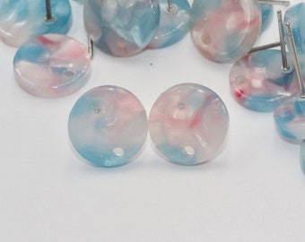 Puede incluir: Dos botones redondos de mármol azul y rosa con un agujero en el centro. Los botones están sobre una superficie blanca.