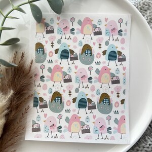 May include: A square, patterned paper with a repeating design of pastel-colored birds, eggs, and flowers. The birds are in shades of pink, blue, and brown, carrying baskets and standing near eggs and flowers. The background is white.