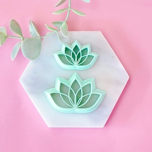 Puede incluir: Dos cortadores de galletas de plástico verde en forma de flores de loto sobre una superficie de mármol blanco.