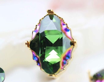 Può includere: Una gemma verde iridescente con una montatura in oro. La gemma è sfaccettata e ha una forma ovale appuntita.