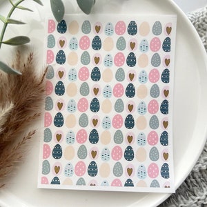 May include: A rectangular sheet with a repeating pattern of Easter eggs and hearts in pastel colors. The eggs are decorated with dots, stripes, and solid colors of pink, blue, and beige. Gold hearts are interspersed throughout the design.
