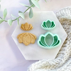 Puede incluir: Un juego de cuatro cortadores de galletas con forma de flor de loto. Dos cortadores son verdes y dos son marrones.