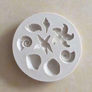 Peut inclure: Moule en silicone blanc avec huit formes différentes de coquillages et d'étoiles de mer. Le moule est conçu pour faire des décorations en pâte à sucre ou en pâte de gomme.