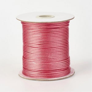 Op de afbeelding: Een spoel levendig roze koord, strak gewikkeld rond een kartonnen kern. Het koord heeft een gladde, licht glanzende textuur. De spoel is ideaal voor knutselen, sieraden maken of andere creatieve projecten.