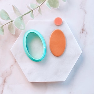 May include: Three oval-shaped acrylic blanks in different sizes. The largest blank is turquoise, the medium blank is orange, and the smallest blank is pink.