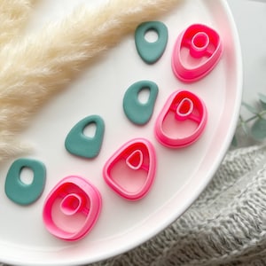 Op de afbeelding: Een wit bord met zes verschillende koekjesvormen. Drie van de vormen zijn roze en drie zijn turquoise.