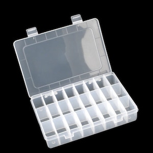 May include: A clear plastic storage box with a hinged lid and multiple compartments. The box is rectangular and has a series of dividers creating small, individual spaces. The lid is open, revealing the interior.