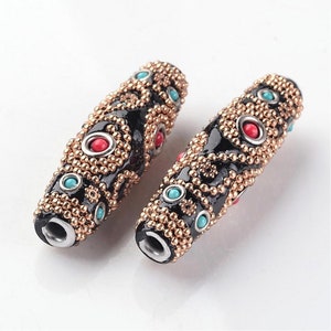 May include: Two black wooden beads with gold and silver accents. The beads are decorated with turquoise and red stones and have a geometric pattern.