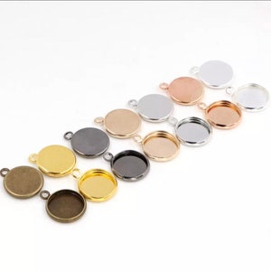 May include: Assortment of round metal pendant trays in various finishes, including gold, silver, bronze, and black. The trays have a smooth, circular surface and a loop at the top for attaching to a chain or cord.