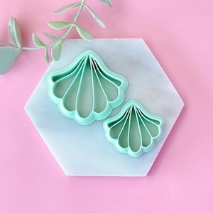 Puede incluir: Dos cortadores de galletas de plástico verde en forma de conchas. La concha más grande está en el fondo y la concha más pequeña está en primer plano.