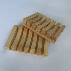 Puede incluir: Dos jaboneras de madera, una apilada sobre la otra. La jabonera superior tiene listones curvos y la jabonera inferior tiene listones rectos.
