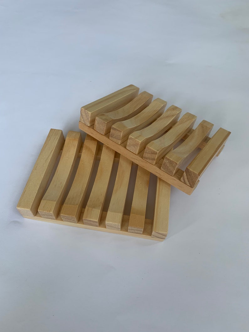 Puede incluir: Dos jaboneras de madera, una apilada sobre la otra. La jabonera superior tiene listones curvos y la jabonera inferior tiene listones rectos.
