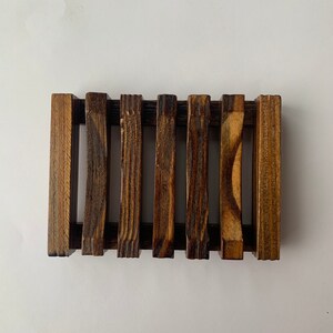 Puede incluir: Un jabonera de madera con un dise&ntilde;o de listones. La jabonera es de color marr&oacute;n oscuro y tiene un aspecto r&uacute;stico.