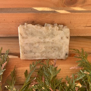 May include: A bar of handmade soap with a light brown color and a speckled appearance. The soap is sitting on a wooden surface.
