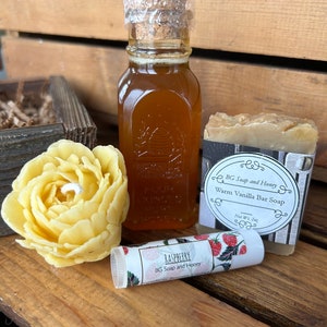 May include: A gift set with a small bottle of honey, a bar of soap, and a lip balm. The soap is labeled "Warm Vanilla Bar Soap" and the lip balm is labeled "Raspberry".