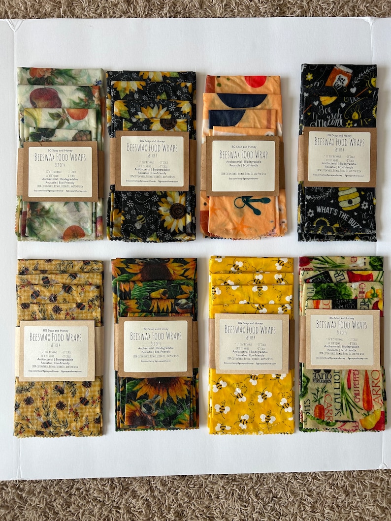 May include: A set of eight beeswax food wraps in various designs. The wraps are made of cotton fabric coated with beeswax, jojoba oil, and tree resin. The designs include sunflowers, bees, and a variety of fruits and vegetables. The wraps are reusable and biodegradable. The text on the labels reads "Beeswax Food Wraps" and "Set of 4".