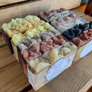 May include: A set of 10 handmade soap bars in a variety of colors and scents, including lavender, charcoal, and citrus. The soaps are packaged in individual boxes with a label that says "Bath & Body Handmade Soaps"