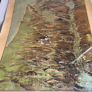 May include: A vintage map of the Holy Land, showing geographical features and place names. The map uses shades of brown, green, and beige, with text labels including "Galilee" and "Judea". The map is framed with a black border.