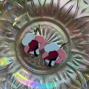 Puede incluir: Un par de pendientes de color rosa y blanco con un diseño de flor roja. Los pendientes están hechos de metal y tienen un cierre de gancho.