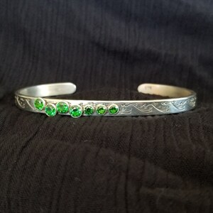 May include: A silver bracelet with a wave design and a row of green gemstones.