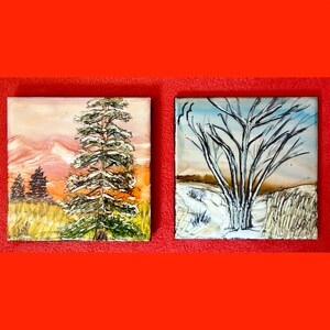 May include: Two square landscape paintings. One shows a tall evergreen tree with snow, set against a sunset sky. The other depicts a bare tree in winter, with a snowy ground and a blue sky.