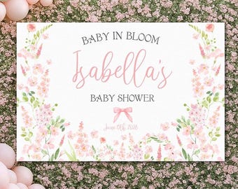 Könnte beinhalten: Eine Babyparty-Kulisse mit dem Text "Baby in Bloom" und "Isabella's Baby Shower" in rosa Schrift. Die Kulisse ist mit floralen Illustrationen und einer rosa Schleife verziert. Ein Ballonbogen in Rosa- und Grüntönen rahmt die Szene ein.