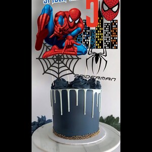 May include: A blue and white drip cake decorated with a Spiderman themed topper. The topper features a red and blue Spiderman figure, a black web, a red Spiderman head, and a red number 5.