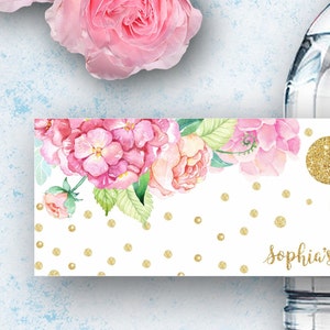 K&ouml;nnte beinhalten: Wasserflaschenetikett mit einem rosafarbenen Blumendesign und goldenen Glitzerpunkten. Der Text "Sophia's Birthday" befindet sich am unteren Rand des Etiketts.