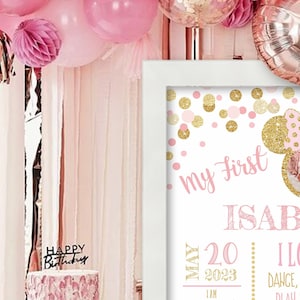 May include: Pink and gold first birthday sign with a photo of a baby girl. The sign says "my first" and "ISABELLA" with a pink and gold Mickey Mouse ears design. The sign also says "MAY 20 2023 I AM" and "I LOVE DANCE, TALK, PLAY WITH MY"