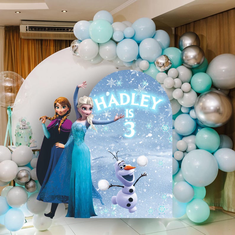 May include: A blue and white Frozen themed party backdrop with a cutout of Elsa and Anna from the movie Frozen. The backdrop also features Olaf, the snowman from the movie. The backdrop is decorated with snowflakes and the text "HADLEY IS 3".