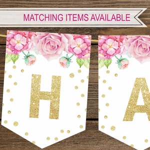 Puede incluir: Una pancarta blanca con dise&ntilde;os florales rosas y letras doradas con brillo que deletrean "HA". La pancarta tiene un fondo blanco con lunares dorados.