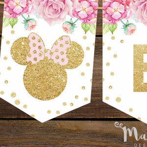Puede incluir: Una pancarta blanca con orejas de Mickey Mouse de purpurina dorada y un lazo rosa. La pancarta tambi&eacute;n tiene una letra "B" de purpurina dorada y un dise&ntilde;o floral con flores rosas y hojas verdes.
