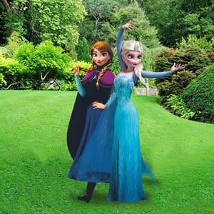 May include: Two female characters from the animated movie Frozen, Elsa and Anna, are dressed in their signature blue and purple dresses. They are standing in a grassy garden setting.