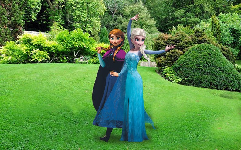 May include: Two female characters from the animated movie Frozen, Elsa and Anna, are dressed in their signature blue and purple dresses. They are standing in a grassy garden setting.