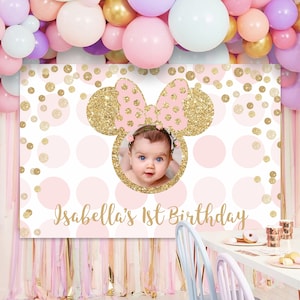 May include: A pink and gold glitter Minnie Mouse themed backdrop with a photo cutout for a child's first birthday. The backdrop has a white background with pink and gold polka dots. The text "Isabella's 1st Birthday" is printed at the bottom of the backdrop.