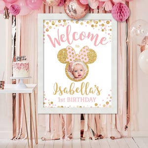 Pu&ograve; includere: Un cartello di benvenuto rosa e oro con una silhouette di testa di Minnie Mouse e una foto di una bambina. Il cartello dice "Benvenuti al 1&deg; compleanno di Isabella" con coriandoli dorati glitterati.