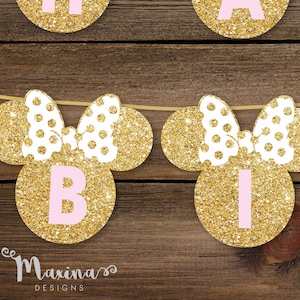 May include: Gold glitter Minnie Mouse ears with pink polka dots and a pink letter "B" in the center. The ears are strung together with a white string.