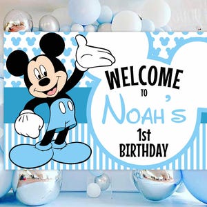 May include: Blue and white Mickey Mouse themed birthday party sign with the text "Welcome to Noah's 1st Birthday".
